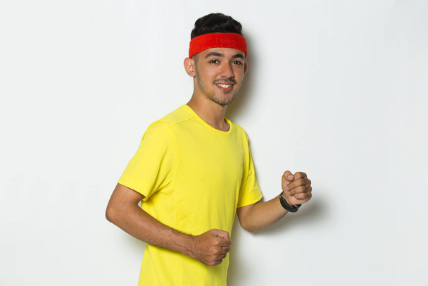 joven hombre deportivo vestido con camiseta amarilla corriendo sobre fondo blanco - Foto, imagen