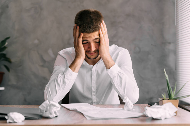 Stress and headache of a man from vasospasm in the office at the workplace working with documents. Bankruptcy and contract for a company manager. The businessman is upset and sad. Business concept. - Photo, Image