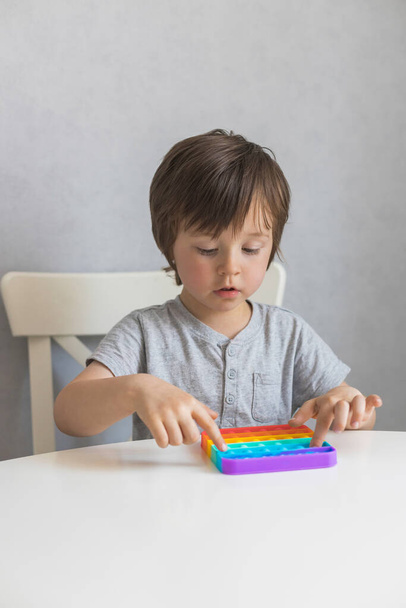 Adorable boy is playing at home with a new trendy silicone pop it toy. Development of sensory motor skills. Kids toys. - Photo, Image