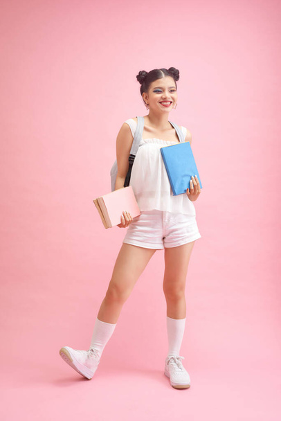 Back to school. Teen girl with books on a bright pink and yellow background - Fotoğraf, Görsel