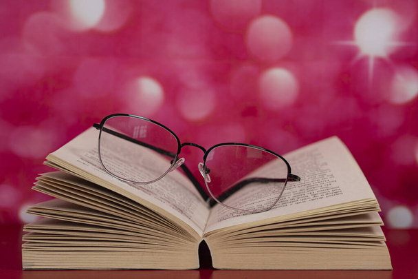 Sayfaların üstünde gözlük olan açık bir kitap. Seçici odak noktaları. Bulanık arkaplan - Fotoğraf, Görsel