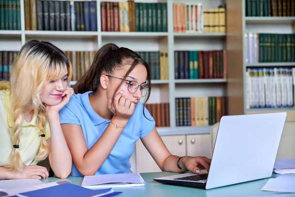 Two girls, students, adolescents 15, 16 years old study in library, using laptop - Фото, зображення