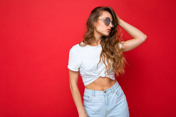 Attractive young blonde woman wearing everyday stylish clothes and modern sunglasses isolated on colorful background wall looking to the side - Φωτογραφία, εικόνα