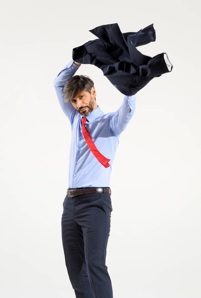 Elegante hombre de negocios que se pone su chaqueta de traje aislada en blanco balanceándola sobre su cabeza mientras inserta sus brazos en las mangas - Foto, Imagen