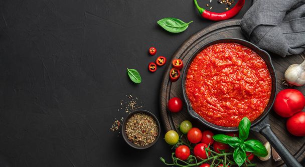 Italiaanse klassieke huisgemaakte saus met basilicum en peper op een zwarte achtergrond. Marinara saus. Kleding voor pasta, pizza. - Foto, afbeelding