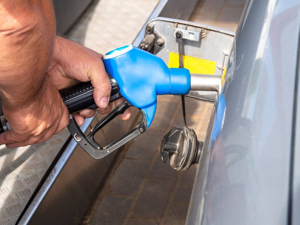 Ένας άντρας κρατάει ένα πιστόλι βενζινάδικου στο ντεπόζιτο. Ένα αρσενικό γεμίζει το ντεπόζιτο του αυτοκινήτου με καύσιμα. - Φωτογραφία, εικόνα