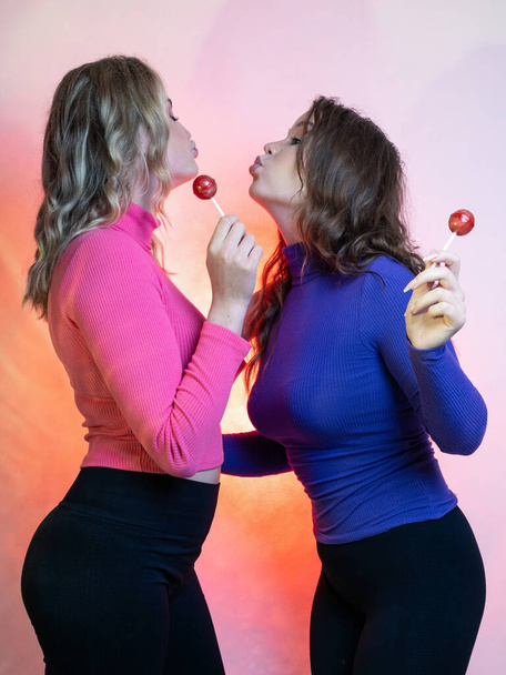 Portrait of twogirlfriends. They are funny, in the hands of lollipops. In a studio . on a pink background. - Foto, afbeelding