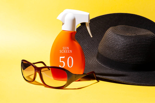 50 bescherming zonnecrème met zonnebril en pamela hoed op gele achtergrond. Zonwering concept, zomer. - Foto, afbeelding