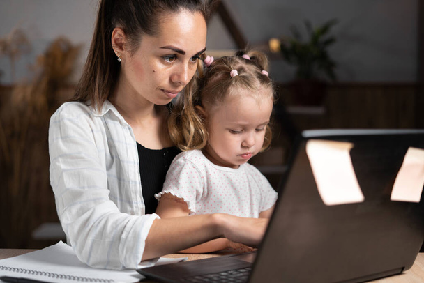 Headshot зосередив увагу на навчанні маленької дівчинки під час домашнього завдання з матір'ю. Ласкава молода мати вчить свою маленьку доньку працювати в ноутбуці. Копіювати простір
. - Фото, зображення