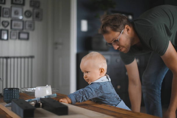 portret van een aantrekkelijke nerd met een bril thuis spelend met een zoon. Schattige kleine jongen. Gelukkig vaderschap - Foto, afbeelding