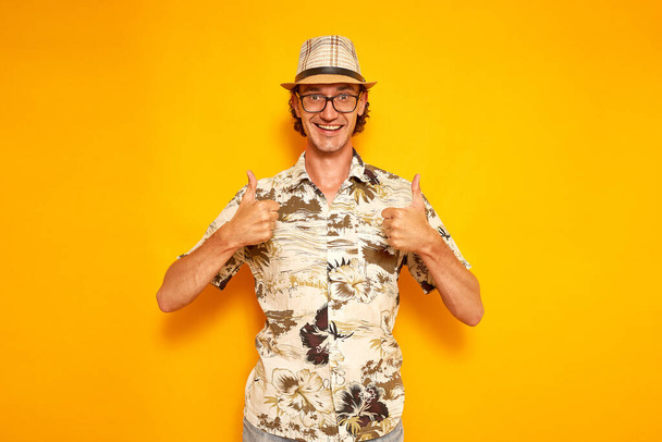 Tatilde dünyayı gezen mutlu gülümseyen adam Hawaii gömlekli şapka gözlükleri başarıya seviniyor izole edilmiş sarı arka plan her şeyin iyi olduğunu gösteriyor. konsept eğlencesi, millet. - Fotoğraf, Görsel