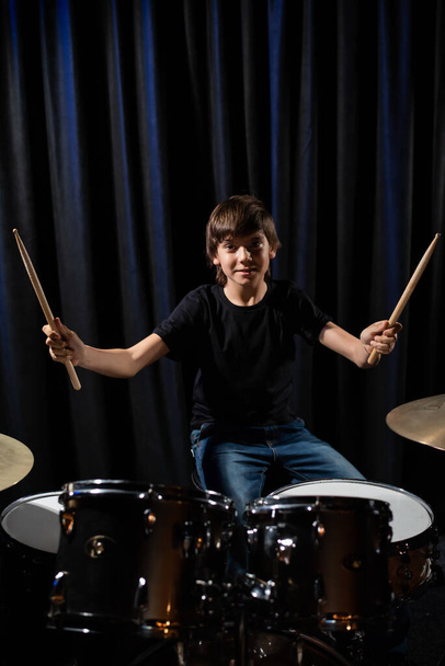 The boy learns to play the drums in the studio on a black background. Music school student - Foto, Imagem