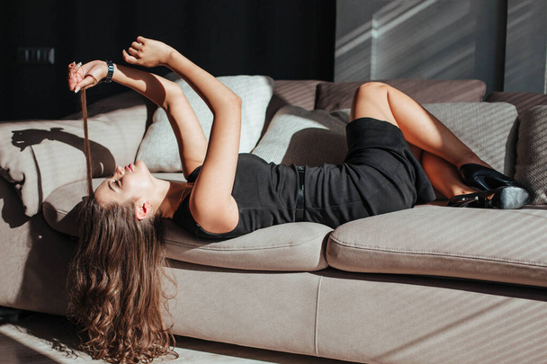 kaunis nainen mustassa mekossa makaa sohvalla ja koskettaa hiuksiaan - Valokuva, kuva