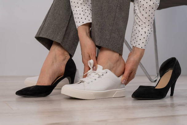 Close-up business woman takes off her shoes puts on white leather sneakers. - Φωτογραφία, εικόνα