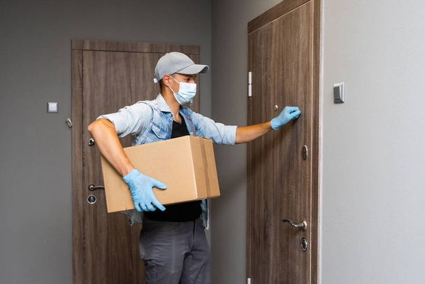 Entrega a domicilio hombre caja de compras con guantes y máscara protectora entrega de paquetes en la puerta - Foto, imagen