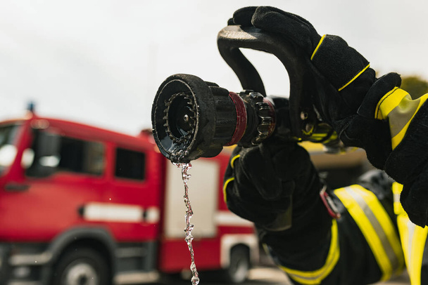 Feuerwehrmann im Einsatz mit Wasserschlauch vor Löschfahrzeug bereit zum Löschen. Nahaufnahme - Foto, Bild