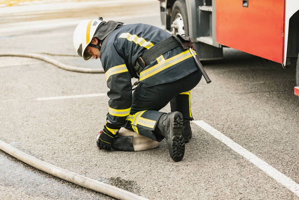 Один молодой пожарный, одетый в униформу с водяным шлангом у пожарной машины, готовый к развертыванию - Фото, изображение
