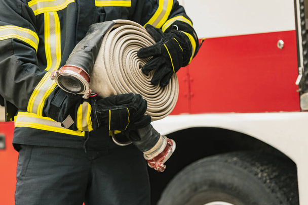 Imagem cortada. Um bombeiro vestido de uniforme com mangueira de água no caminhão de bombeiros pronto para implantação - Foto, Imagem
