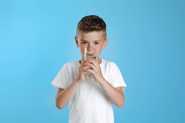 Cute little boy drinking water from glass on light blue background - Foto, Imagen