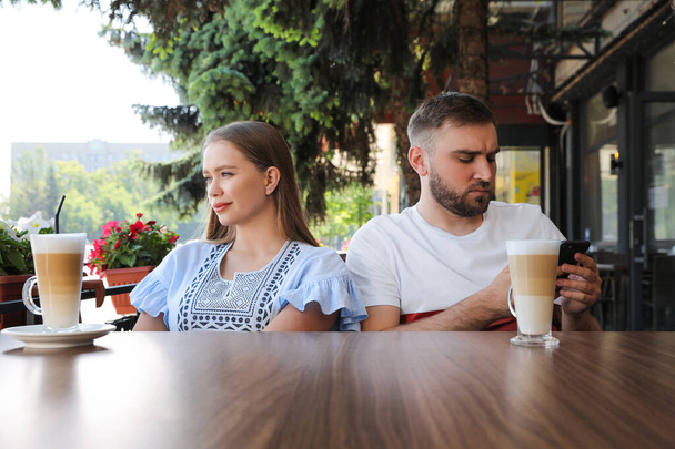 Young man with smartphone ignoring his girlfriend in outdoor cafe. Boring date - Foto, Imagen