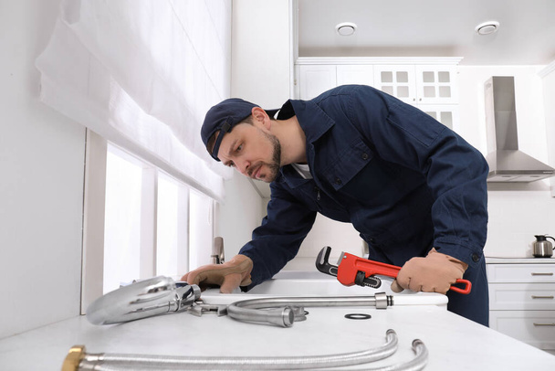 Professional plumber fixing water tap in kitchen - Fotó, kép