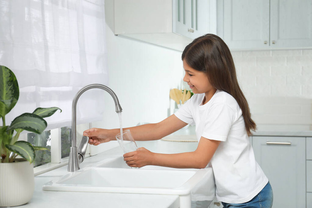 Girl filling glass with water from tap in kitchen - Φωτογραφία, εικόνα