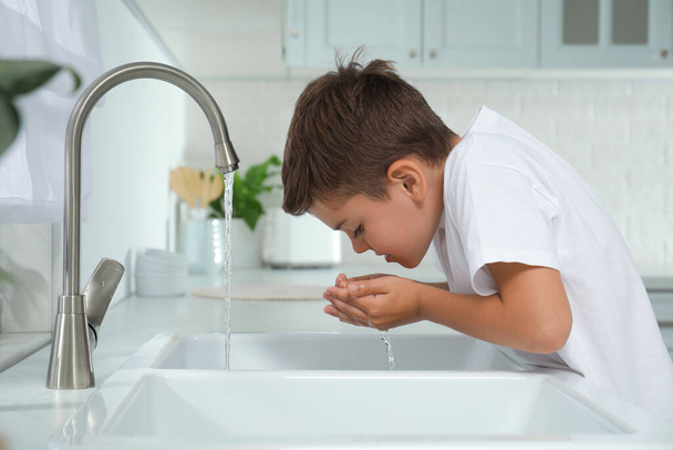 Boy drinking tap water over sink in kitchen - Фото, изображение