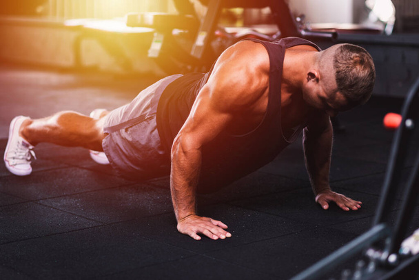 Sport young athletic man doing push-up. Muscular and strong guy exercising at a gym.Strength and motivation concept.Young handsome man in sportswear doing push ups at gym.Selective focus.Toned. - Photo, Image