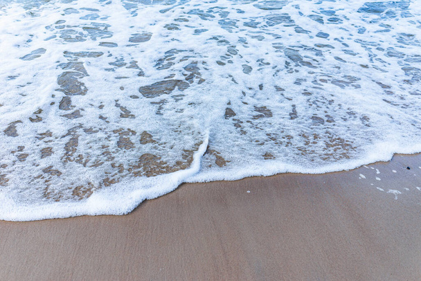Морская волна на песчаном пляже с белой пеной. Вид сверху на волну, ломающуюся на песке.. - Фото, изображение