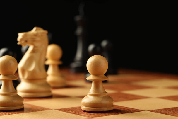 Chessboard with game pieces on black background - Φωτογραφία, εικόνα