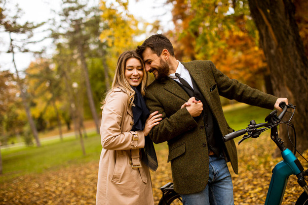 Hermosa pareja joven en el parque de otoño con bicicleta eléctrica - Foto, imagen