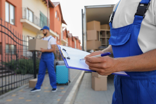 Moving service workers outdoors, unloading boxes and checking list - Φωτογραφία, εικόνα