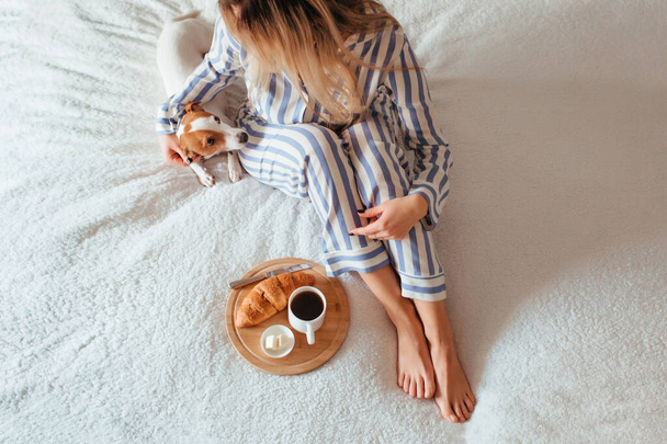 πρωινό στο κρεβάτι κρουασάν και καφέ. Δίπλα της είναι μια γυναίκα με πιτζάμες.  - Φωτογραφία, εικόνα
