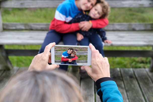 Мама фотографує своїх двох дітей за допомогою мобільного телефону. - Фото, зображення