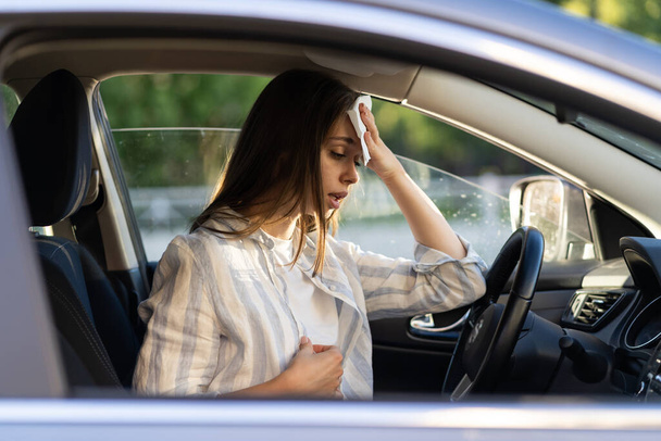 Woman driver being hot during heat wave in car, suffering from hot weather wipes sweat from forehead - Photo, Image