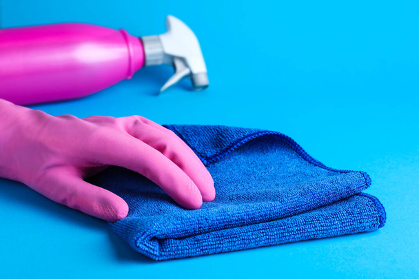 Woman in pink rubber gloves with microfiber cloth and detergent on light blue background, closeup - Foto, Bild