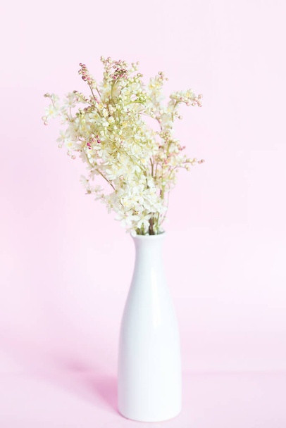 Bouquet of meadowsweet (Latin Filipndula), jasmine and wild roses in a vase on a pink background. - Foto, imagen