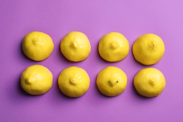 Cut lemons symbolizing women's breasts and one with nipple piercing on purple background, flat lay - Zdjęcie, obraz