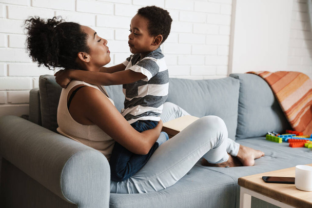 Black happy mother and son hugging and making fun while sitting on sofa at home - Fotoğraf, Görsel
