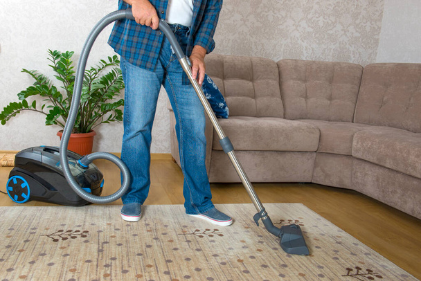 A man vacuums the carpet in his room. - 写真・画像