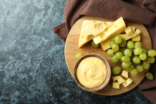 Tabuleiro com molho de queijo, uva e queijo sobre mesa de fumaça preta com toalha de cozinha - Foto, Imagem