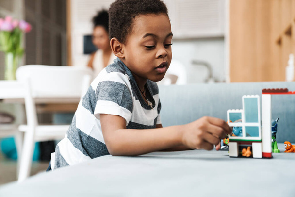 Black boy in t-shirt playing with toy on couch at home - Foto, imagen
