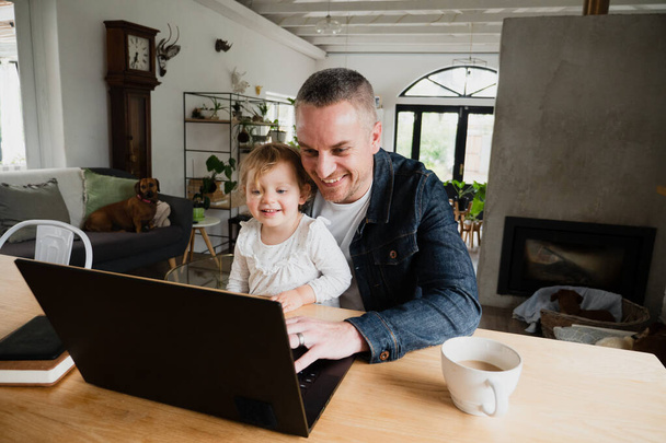 Father and daughter laughing at funny videos on laptop bonding spending family time together. - Foto, imagen