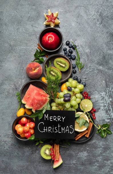 Christmas tree made of fruits on dark background. New Year Holidays concept. Top view, flat lay - Фото, зображення