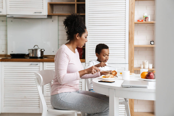 Black mother and son having breakfast together while sitting at home - Fotó, kép