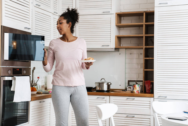 Black woman using microwave while preparing her breakfast at home - 写真・画像