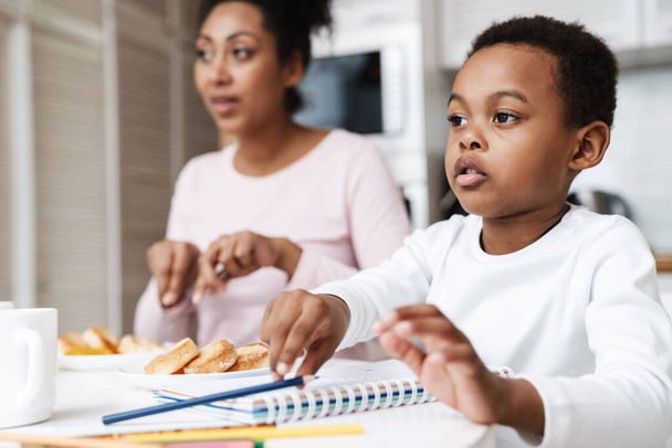 Black boy drawing while having breakfast with her mother at home - Fotoğraf, Görsel