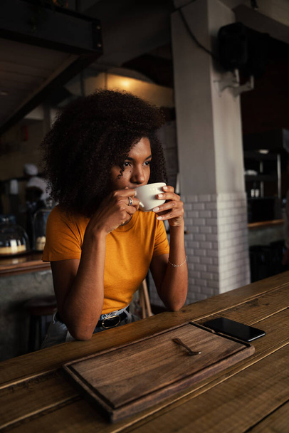 Mixed race female drinking hot coffee sitting in trendy cafe  - Fotó, kép