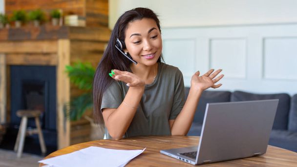 Asian woman during online video call in front of a laptop monitor. She actively gestures while communicating with interlocutor. Format 16x9. - Foto, Imagem