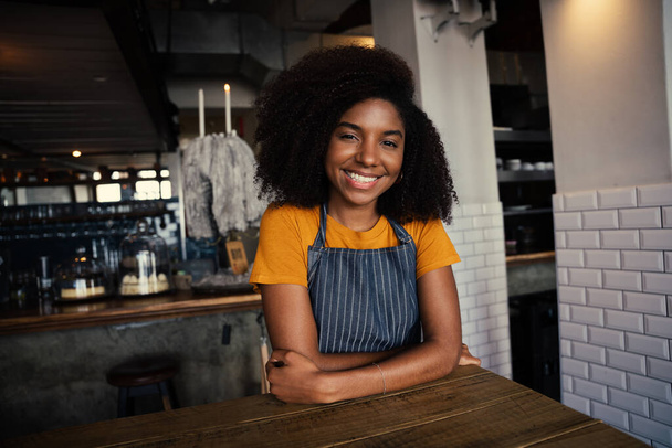 Hermosa camarera femenina de raza mixta con delantal sentado en la mesa de café en el café funky  - Foto, imagen